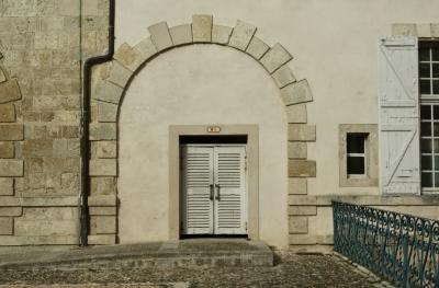photograph “II.2025” par David Farreny — www.farreny.net — France, Occitanie, Gascogne, Gascony, Lomagne, Gers, Lectoure, mairie, city hall, town hall, cour, courtyard, pierre, stone, mur, wall, pavés, cobblestones, fenêtres, windows, rambarde, guardrail, métal, metal, bois, wood, gouttière, drainpipe, arche, arch, arcade, toilettes, public, toilets, WC, portes, doors, poignées, handles, plaque, plate