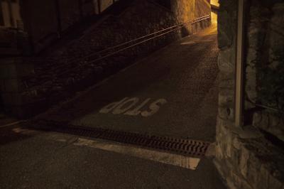 photograph “VII.2023 — At night” par David Farreny — www.farreny.net — Andorre, Andorra, Canillo, rue, street, ruelle, alley, pente, slope, bitume, blacktop, asphalte, asphalt, nuit, night, soir, evening, rampe, railing, banister, métal, metal, carrefour, crossing, stop, inscription, sol, ground, peinture, paint, angle, corner, coin, pierre, stone, mur, wall, immeuble, bâtiment, building, lumière, light, jaune, yellow