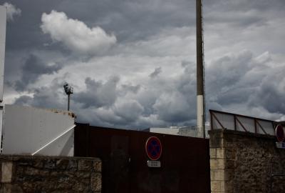 photograph “V.2014 — Whatever” par David Farreny — www.farreny.net — France, Occitanie, Aveyron, Rouergue, Rodez, stade, stadium, mur, wall, pierre, stone, portail, gate, métal, metal, panneaux, signs, routiers, roadsigns, projecteurs, floodlights, poteaux, poles, posts, ciel, sky, nuages, clouds, entrée, entrance, orage, storm