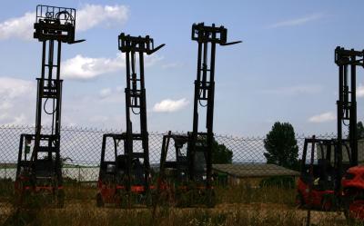 photograph “VI.2005” par David Farreny — www.farreny.net — France, Occitanie, Aveyron, Rouergue, Rodez, chariots élévateurs, forklifts, fourches, forts, métal, metal, véhicules, vehicles, grillage, fencing, clôture, fence, ciel, sky, nuages, clouds, herbe, grass