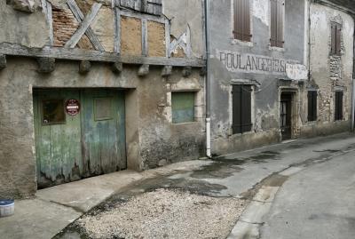photograph “I.2024” par David Farreny — www.farreny.net — France, Occitanie, Tarn-et-Garonne, Montricoux, village, rue, street, maisons, houses, vieux, old, délabré, dilapidated, garage, portail, gate, murs, walls, boulangerie, bakery, bitume, blacktop, asphalte, asphalt, gouttière, drainpipe, métal, metal, enseigne, sign, fermé, closed down, pierre, stone, ciment, cement, brique, brick, panneau, fenêtres, windows, volets, shutters, bois, wood