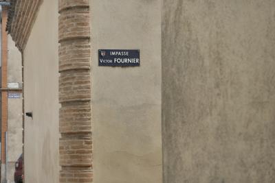 photograph “III.2024” par David Farreny — www.farreny.net — France, Occitanie, Tarn-et-Garonne, Caussade, ville, city, rue, street, murs, walls, beige, angle, coin, corner, plaques, plates, impasse Victor-Fournier, place Victor-Fournier, métal, metal, brique, brick, génoises, voiture, car, gouttière, drainpipe