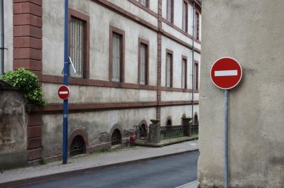 photograph “V.2014” par David Farreny — www.farreny.net — France, rue, street, sens interdit, one-way, panneaux, signs, roadsigns, mur, ciment, cement, métal, metal, rouge, red, bâtiment, building, immeuble, coin, corner, angle, soupiraux, basement windows, fenêtres, windows, volets, shutters, plante, plant, trottoir, pavement, bitume, blacktop, asphalte, asphalt, barrière, guardrail, rambarde, gouttière, drainpipe, ville, city, Occitanie, Aveyron, Rouergue, Rodez