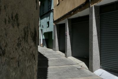 photograph “V.2023 — Faces of home, 180” par David Farreny — www.farreny.net — Espagne, Spain, España, Espanya, Catalogne, Catalonia, Cataluña, Catalunya, Lérida, Lleida, La Seu d'Urgell, rue, street, ruelle, alley, mur, wall, garages, portails, gates, métal, metal, pierre, stone, béton, concrete, porte, door, immeubles, buildings, bâtiments, câbles, cables, fils, wires, ombre, shadow, fenêtres, windows, domicile, home