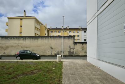 photograph “VII.2024 — Faces of home, 219” par David Farreny — www.farreny.net — France, Occitanie, Gascogne, Gascony, Gers, Auch, immeubles, bâtiments, buildings, béton, concrete, murs, wall, parois, voiture, car, rue, street, bitume, blacktop, asphalte, asphalt, lampadaire, lamp, herbe, grass, trottoir, pavement, fenêtres, windows, balcons, balconies, poubelle, bin, trash, ciel, sky, nuages, clouds, cheminées, chimneys, toit, roof