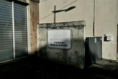 photograph “XII.2023 — Whatever” par David Farreny — www.farreny.net — France, Occitanie, Tarn-et-Garonne, Caussade, bâtiment, immeuble, building, béton, concrete, mur, wall, magasin, shop, atelier, workshop, store, métal, metal, portail, gate, boîte à lettres, mailbox, letterbox, câble, cable, fil, wire, ombre, shadow, lampadaire, lamp, trottoir, pavement, brique, brick, verre, vitre, glass, baie, window, panneau, sign, board, motocycles, motorcycles, vente, sale, entretien, réparation, maintenance, repair