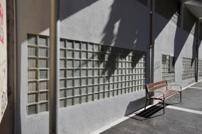 photograph “X.2021” par David Farreny — www.farreny.net — Andorre, Andorra, Escaldes-Engordany, bâtiment, immeuble, building, béton, concrete, poteaux, posts, poles, mur, wall, tags, graffitis, banc, bench, trottoir, pavement, bitume, asphalte, blacktop, asphalt, blocs de verre, briques de verre, glass blocks, glass bricks, carrés, squares, ombres, shadows, balcons, balconies