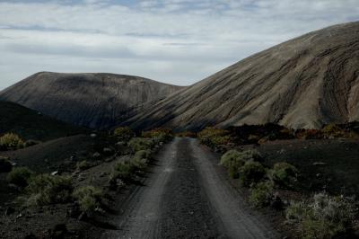 photograph “V.2016 — Lancerotte, 34” par David Farreny — www.farreny.net — Espagne, Spain, España, Canaries, Canarias, Canary, Lanzarote, Lancerotte, île, island, volcans, volcanoes, montagnes, mountains, route, road, poussière, dust, paysage, landscape, nature, désert, desert, lave, lava, buissons, shrubs, piste, track, nuages, clouds, Tinajo