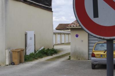 photograph “III.2021” par David Farreny — www.farreny.net — France, Occitanie, Gascogne, Gascony, Gers, Éauze, ville, city, bourgade, town, immeuble, bâtiment, building, béton, concrete, mur, wall, garages, toits, roofs, tuiles, tiles, tôle ondulée, corrugated iron, voiture, car, métal, metal, Renault, Twingo, panneau, routier, sign, roadsign, plaque, plate, 216, jaune, yellow, allée, alley, bitume, blacktop, asphalte, asphalt, poubelles, trash cans, conteneurs, containers, garbage, ordures, nuages, clouds, herbe, grass