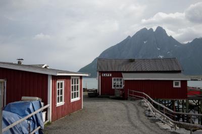 photograph “VII.2017 — Run away to the North, 122” par David Farreny — www.farreny.net — Norvège, Norway, Norge, Norvège du Nord, Nord-Norge, Nordland, Flakstad, Sund, Lofoten, pêche, fishing, port, harbour, village, maisons, houses, café, kafe, enseigne, sign, rambarde, guardrail, bois, wood, bâches, tarpaulins, plastique, plastic, pilotis, piles, mer, sea, eau, water, montagne, mountain, pic, peak, summit, Ølkontinden