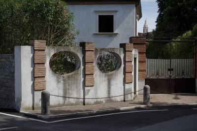 photograph “VIII.2022 — :-)” par David Farreny — www.farreny.net — Italie, Italia, Italy, Toscane, Toscana, Tuscany, Sienne, Siena, Pienza, maison, house, portail, gate, trottoir, pavement, rue, street, mur, wall, brique, brick, béton, concrete, métal, metal, chaîne, chain, arbres, trees, clocher, bell tower, trous, holes, smiley