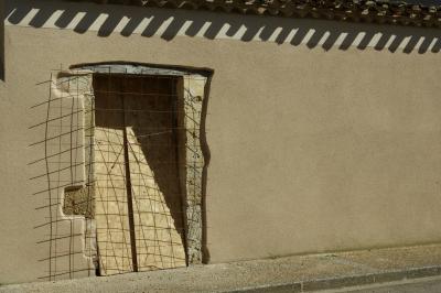photograph “III.2025” par David Farreny — www.farreny.net — France, Occitanie, Gascogne, Gascony, Gers, Fleurance, ville, city, bourgade, town, rue, street, mur, wall, porte, door, tuiles, tiles, pierre, stone, condamnée, condemned, plaques, bois, wooden, plates, grillage, fencing, grille, fence, métal, metal, trottoir, pavement, ombres, shadows, closed, fermé, chantier, construction site
