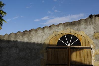 photograph “X.2020 — Faces of home, 109” par David Farreny — www.farreny.net — France, bâtiment, building, maison, house, tuiles, tiles, portail, gate, bois, wood, baie, fenêtre, window, arc, arch, arche, planches, planks, pierre, stone, crépi, roughcast, palmier, palm tree, arbre, tree, ciel, sky, automne, autumn, fall, village, ondulation, domicile, home, Occitanie, Gascogne, Gers, Barran