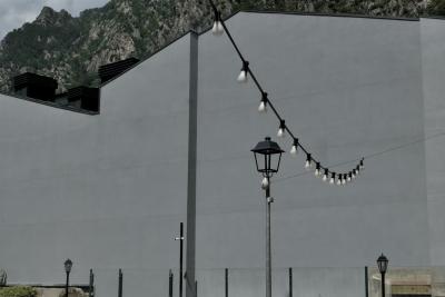 photograph “VI.2021” par David Farreny — www.farreny.net — Andorre, Andorra, Andorre-la-Vieille, Andorra la Vella, ville, city, capitale, capital, mur, wall, béton, concrete, montagne, mountain, gris, grey, gray, lampadaires, street lamps, grillage, fence, clôture, fencing, bâtiment, building, rocher, rock, lampes, lamps, ampoules, bulbs, décoration, decoration, ornemental, cheminées, chimneys, câbles, cables, fil, wire, caméra, vidéo, video, camera, métal, metal, Pyrénées, Pyrenees