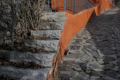 photograph “I.2023” par David Farreny — www.farreny.net — Andorre, Andorra, Encamp, ruelle, alley, pierre, stone, escalier, stairs, staircase, marches, steps, terrasse, terrace, rambarde, guardrail, feuilles, leaves, mortes, dead, mur, wall, orange, rampe, banister