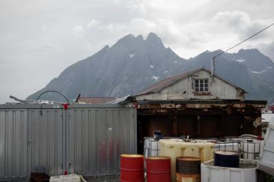 photograph “VII.2017 — Run away to the North, 254. Both roofs” par David Farreny — www.farreny.net — Norvège, Norway, Norge, Norvège du Nord, Nord-Norge, Nordland, Flakstad, Sund, Lofoten, pêche, fishing, port, harbour, harbor, matériel, equipment, montagne, mountain, pic, peak, summit, nuages, clouds, bâtiment, building, toit, roof, container, conteneur, métal, metal, bidons, cans, câble, cable, fil, wire, rouille, rust, béton, concrete