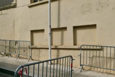photograph “III.2021” par David Farreny — www.farreny.net — France, bâtiment, immeuble, building, mur, wall, trottoir, pavement, rue, street, pierre, stone, béton, concrete, fenêtres, windows, murées, walled up, barrières, guardrails, métal, metal, poteau, pole, post, câbles, wires, fils, cables, ombre, shadow, enseigne, sign, enlevée, removed, magasin, shop, store, supermarket, supermarché, épicerie, grocery, Spar, lettres, letters, caractères, characters, SP, Occitanie, Gascogne, Gers, Éauze