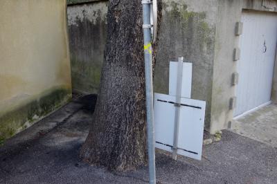 photograph “XII.2020” par David Farreny — www.farreny.net — France, Occitanie, Gard, Castillon-du-Gard, village, garage, portail, gate, rue, street, arbre, tree, panneaux, signs, panneau, routier, road, sign, métal, metal, ciment, cement, tronc, trunk, coin, corner, angle, bois, wood, mur, wall, bitume, blacktop, asphalte, asphalt, humidité, dampness, humide, damp, année, year, 1958, croix, jaune, yellow, cross