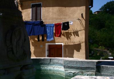 photograph “VIII.2008 — La bella estate” par David Farreny — www.farreny.net — Italie, Italia, Italy, Toscane, Toscana, Tuscany, Sienne, Siena, Asciano, Crete senesi, viillage, ville, town, fontaine, fountain, eau, water, pierre, stone, rocher, rock, sculpture, bas-relief, low relief, maison, house, fenêtre, window, porte, door, linge, étendu, hung, clothes, clothesline, étendoir, fils, wires, coin, corner, angle, volets, shutters, persiennes, arbres, trees, chaleur, heat, warm, chaud, été, summer, canicule, heatwave, Pavese, Le bel été, The beautiful summer, laundry