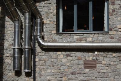 photograph “II.2023” par David Farreny — www.farreny.net — Andorre, Andorra, Canillo, immeuble, building, bâtiment, mur, wall, pierre, tuyaux, pipes, métal, metal, grille, aeration, grid, fenêtre, window, verre, vitre, glass, ampoules, bulbs, spirales, spirals, lumière, light, rideaux, curtains