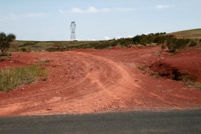 photograph “VIII.2011” par David Farreny — www.farreny.net — France, pylône, électrique, electricity, pylon, métal, metal, route, road, herbe, grass, terre, sol, rouge, red, earth, soil, arbuste, shrub, cailloux, stones, vide, empty, emptiness, bitume, asphalte, asphalt, blacktop, traces, tracks, croisement, carrefour, crossroads, câbles, cables, fils, wires, virage, courbe, bend, curve, paysage, landscape, Occitanie, Rouergue, Aveyron, Camarès, rougier