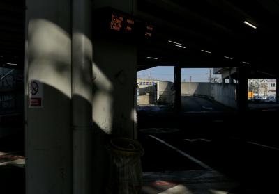 photograph “XII.2023 — Before the non-departure” par David Farreny — www.farreny.net — France, Occitanie, Haute-Garonne, Toulouse, Matabiau, gare routière, bus station, vide, empty, béton, concrete, pilier, pillar, plafond, ceiling, néon, tubes, neon, lumières, lights, poubelle, bin, trash, can, bag, garbage, plastique, plastic, jaune, yellow, tuyau, pipe, panneau, défense de fumer, no smoking, board, horaires, hours, bus, cars, autocars, autobus, Flixbus, Lyon, Porto, bitume, blacktop, asphalte, asphalt, rampe, ramp, voitures, parking, car park, câbles, cables, fils, wires, bâtiments, buildings, station de lavage, wash station, rouleaux, rollers, flèche, arrow