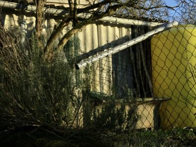 photograph “II.2015” par David Farreny — www.farreny.net — France, Occitanie, Aveyron, Rouergue, Balsac, hiver, winter, jardin, garden, grillage, fencing, clôture, fence, métal, metal, tôle ondulée, corrugated iron, arbre, tree, haie, hergé, tuyau, pipe, gouttière, cutter, cuve, citerne, tank, plastique, plastic, jaune, yellow, ciment, cement
