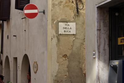 photograph “VIII.2022” par David Farreny — www.farreny.net — Italie, Italia, Italy, Toscane, Toscana, Tuscany, Sienne, Siena, Pienza, maison, house, bâtiment, building, ruelle, alley, via della Buca, pierre, stone, fenêtres, windows, volets, shutters, panneau, sign, roadsign, sens interdit, no way, plaque, plate, distributeur, ATM, 29, portes, doors, touristes, tourists, femmes, women, fils, wires, câbles, cables