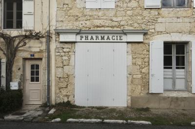 photograph “I.2025 — Obsolete health” par David Farreny — www.farreny.net — France, Occitanie, Gascogne, Gascony, Lomagne, Gers, Saint-Clar, village, rue, street, maisons, houses, pierre, stone, beige, pharmacie, pharmacy, drugstore, enseigne, sign, vieux, old, fermé, closed down, fenêtres, windows, volets, shutters, bois, wood, porte, door, plaque, plate, numéro, number, 7, boîte aux lettres, mailbox, postbox, gouttière, drainpipe, métal, metal, lierre, ivy, hiver, winter, haie, hedge, vitre, verre, glass, trottoir, pavement, bitume, blacktop, asphalte, asphalt, dépression, depression