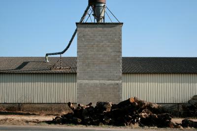 photograph “III.2012” par David Farreny — www.farreny.net — France, usine, factory, industrie, industry, tôle ondulée, corrugated iron, parpaings, breeze-blocks, tour, tower, tuyau, conduit, pipe, métal, metal, bois, wood, tronçons, sections, bûches, logs, grumes, timbers, lumbers, tas, pile, heap, Occitanie, Rouergue, Aveyron, Bozouls