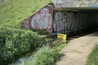 photograph “IV.2024” par David Farreny — www.farreny.net — France, Occitanie, Tarn-et-Garonne, Caussade, Monteils, parc de la Lère, tunnel, piétons, pedestrians, pont, bridge, béton, concrete, herbe, grass, canal, channel, eau, water, chemin, path, tags, graffitis, signatures, laid, ugly, laideur, ugliness, panneau, sign, routier, roadsign, métal, metal, tombé, fallen, renversé, overturned, de camions, trucks, lorries