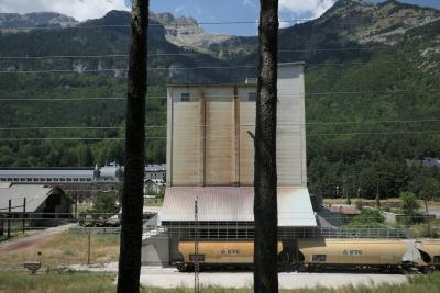 photograph “VIII.2018” par David Farreny — www.farreny.net — Espagne, Spain, España, Aragon, Aragón, Huesca, Jacetania, Canfranc, gare, estación, montagnes, mountains, Pyrénées, Pyrenees, silo, béton, concrete, train, wagons, cars, fret, freight, VTG, voie ferrée, railroad, bâtiments, buildings, forêt, forest, ville, city, arbres, trees, troncs, trunks, câbles, cables, fils, wires, métal, metal, herbe, grass, industrie, industry, sommets, tops