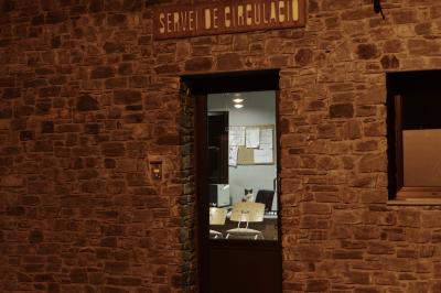 photograph “VII.2023 — Night permanence” par David Farreny — www.farreny.net — Andorre, Andorra, Canillo, police, circulation, traffic, enseigne, sign, Servei de circulació, bureau, office, porte, door, verre, vitre, glass, mur, pierre, stone, fenêtre, window, sonnette, doorbell, desk, chaises, chairs, imprimante, printer, tableau, liège, cork, board, papier, paper, feuilles, sheets, lampes, lamps, chat, cat, animal, permanence