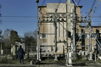 photograph “XII.2023 — Network culture” par David Farreny — www.farreny.net — France, Occitanie, Tarn-et-Garonne, Caussade, ville, city, bourgade, town, building, bâtiment, gare, station, ferroviaire, train, railway, béton, concrete, structure, métal, metal, poteaux, posts, poles, lampadaire, lamp, câbles, cables, fils, wires, quai, platform, arbres, trees, électricité, electricity, voyageuse, traveller, femme, woman, bagages, luggage, grillage, clôture, fence, fencing, caténaires, catenaries, ombres, shadows, profusion