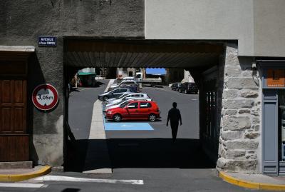 photograph “VII.2011 — Avenue du Président-Pompidou” par David Farreny — www.farreny.net — France, Auvergne, Cantal, Chaudes-Aigues, rue, street, place, square, parking, car park, passage, passageway, voitures, cars, avenue du Président-Pompidou, Pompidou, passant, passer-by, piéton, pedestrian, panneaux, signs, routiers, roadsigns, agence, immobilière, immobilier, property, real estate, agency, trottoir, pavement, mur, wall, pierre, stone, ciment, cement, vitrine, window, 305 m, ville, city, village, magasins, shops, ombre, shadow, tunnel