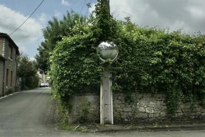 photograph “V.2025 — Where you been” par David Farreny — www.farreny.net — France, Occitanie, Tarn-et-Garonne, Septfonds, village, rue, street, angle, coin, corner, maison, house, muret, low wall, haie, hedge, poteau, post, pole, câble, cable, fil, wire, miroir, mirror, reflet, reflection, trottoir, pavement, bitume, blacktop, asphalte, asphalt, voitures, cars, feuillage, foliage, feuilles, leaves, nuages, clouds, pierres, stones, arbres, trees, fenêtres, windows, croisement, crossing