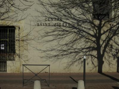 photograph “XII.2016” par David Farreny — www.farreny.net — France, Occitanie, Gascogne, Gers, Aruch, centre Saint-Pierre, lettres, letters, caractères, characters, mur, wall, beige, arbre, tree, ombre, shadow, branches, plots, béton, concrete, pads, porte, door, grille, railings, métal, metal, fenêtre, window, hiver, winter, pierre, stone, trottoir, pavement