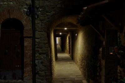 photograph “X.2019” par David Farreny — www.farreny.net — Italie, Italia, Italy, Toscane, Toscana, Tuscany, Sienne, Siena, Casole d'Elsa, soir, evening, nuit, night, village, rue, street, ruelle, alley, tunnel, pierre, stone, brique, brick, médiéval, medieval, angle, coin, corner, pénombre, darkness, sombre, dark, lumière, light, passage, portes, doors, arches, arcs, archs, lampes, lamps, dallage, paving, câbles, cables, fils, wires, plaque, plate, numéro, number, 47, sonnette, doorbell
