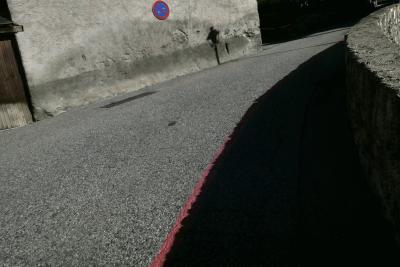 photograph “X.2023 — Whatever” par David Farreny — www.farreny.net — Andorre, Andorra, Canillo, rue, street, bitume, blacktop, asphalte, asphalt, mur, wall, muret, low wall, ombre, shadow, panneau, sign, routier, roadsign, interdiction de stationner, no parking, lampadaire, lamp, portail, gate, bois, wood, ligne, line, peinture, paint, rouge, red, pierre, stone