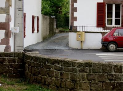 photograph “IV.2013 — Faces of home, 72” par David Farreny — www.farreny.net — France, Aquitaine, Pyrénées-Atlantiques, Pays basque, village, rue, street, voiture, car, rouge, red, volets, shutters, bois, wood, fenêtres, windows, muret, low wall, boîtes à lettres, postbox, letterbox, mailbox, poteau, post, pierre, stone, herbe, grass, chemin, path, passage, Peugeot, 205, way, alley, coin, corner, angle, maisons, houses, jardin, garden, arbres, trees, haie, hedge, gravier, gravel, passage piétons, zebra crossing, métal, metal, domicile, home